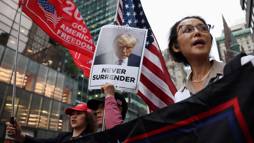 A supporter holds up Trump's mugshot with the words 'never surrender'.