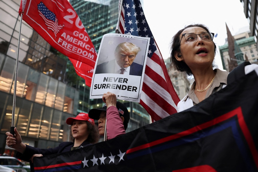 A supporter holds up Trump's mugshot with the words 'never surrender'.