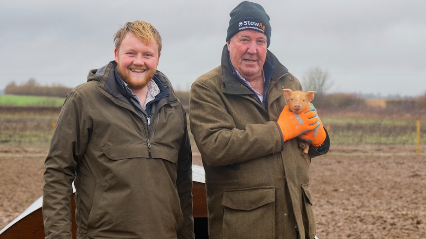 Two men in farming clothes stand in a field in miserable UK weather