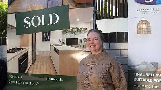 a woman in front of a sold sign out the front of an apartment block with a real estate agent