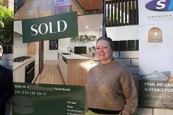 a woman in front of a sold sign out the front of an apartment block with a real estate agent