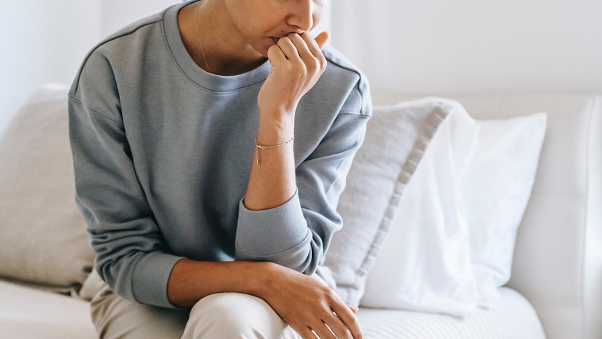 Woman sitting on her bed looking upset, for a story about looking after yourself when sexual assault makes headlines.