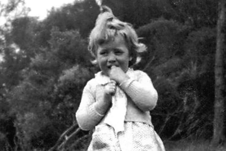 Black and white photo of a young girl wearing a dress, standing on grass