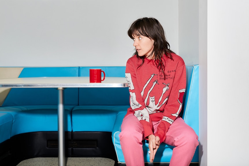 A 2021 press shot of Courtney Barnett seated at a diner booth looking left