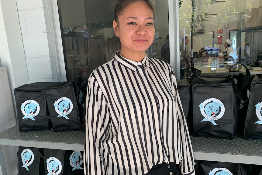 An Asian woman smiles. She is wearing a black and white striped shirt and is standing in front of her branded chiller bags