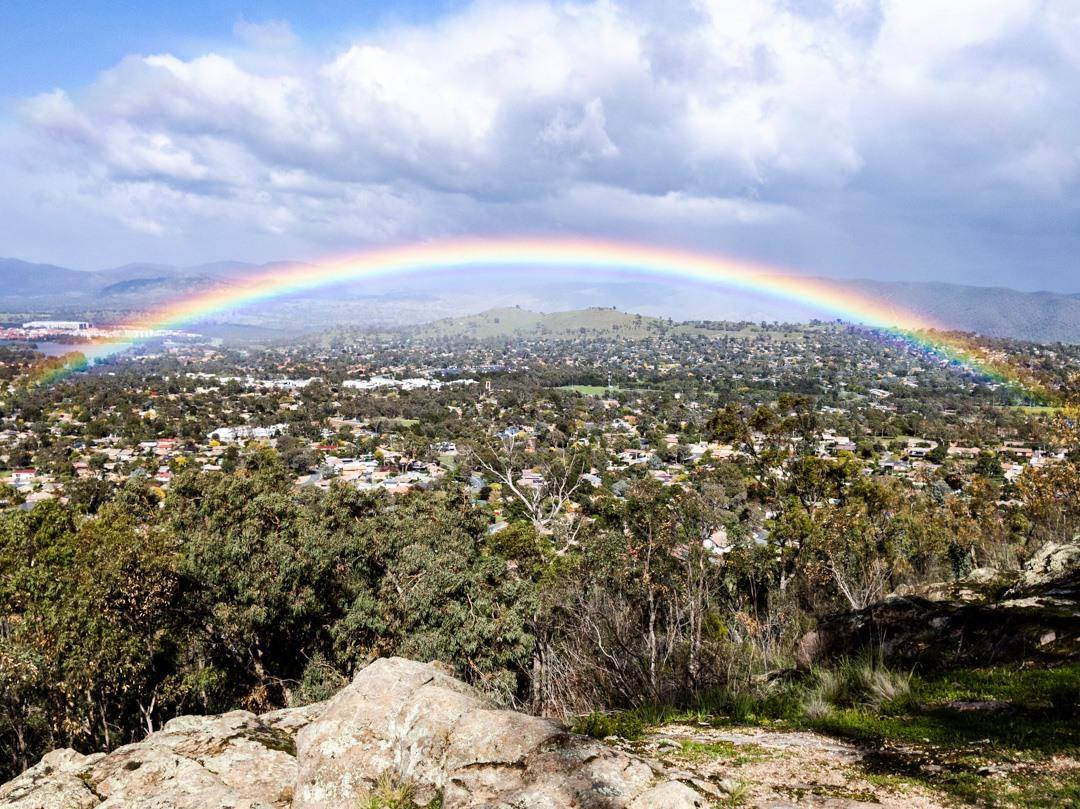 A rainbow over Canberra's hills with houses in the background.