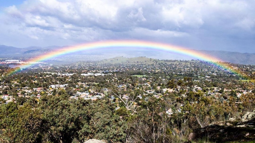 A rainbow over Canberra's hills with houses in the background.