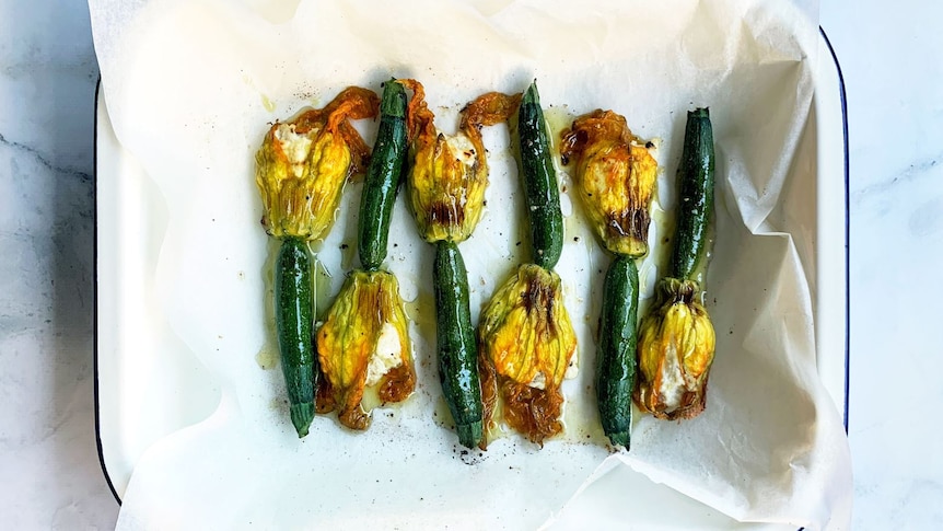 A cooking tray with 6 stuffed yellow and green zucchini flowers that have come out of the oven