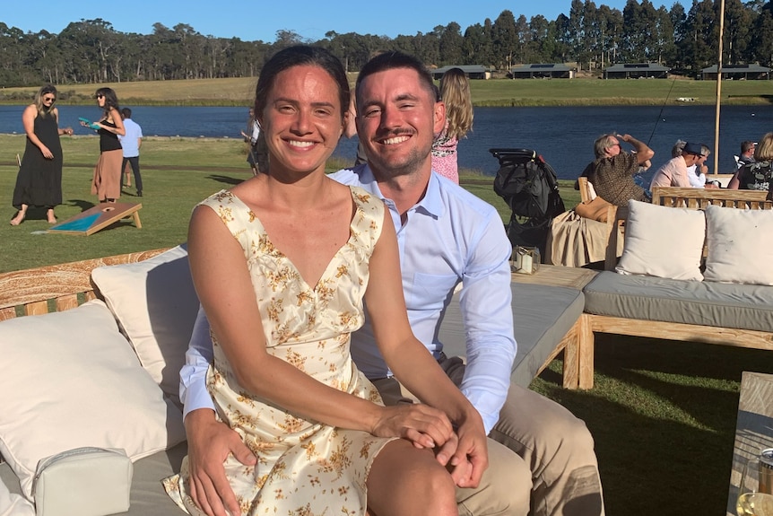 A young couple in formal attire smile at the camera. They are outside.