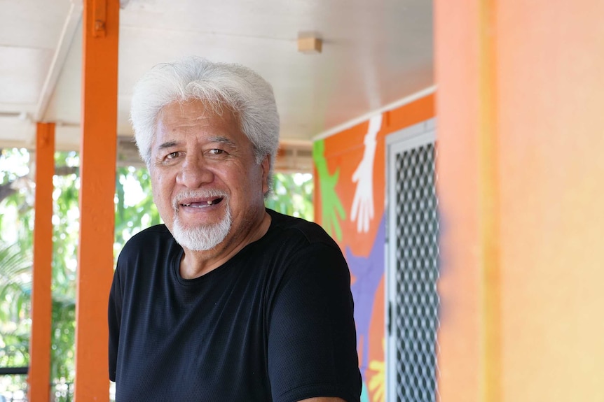 Portrait of Maori man with white hair standing on the porch of an orange building