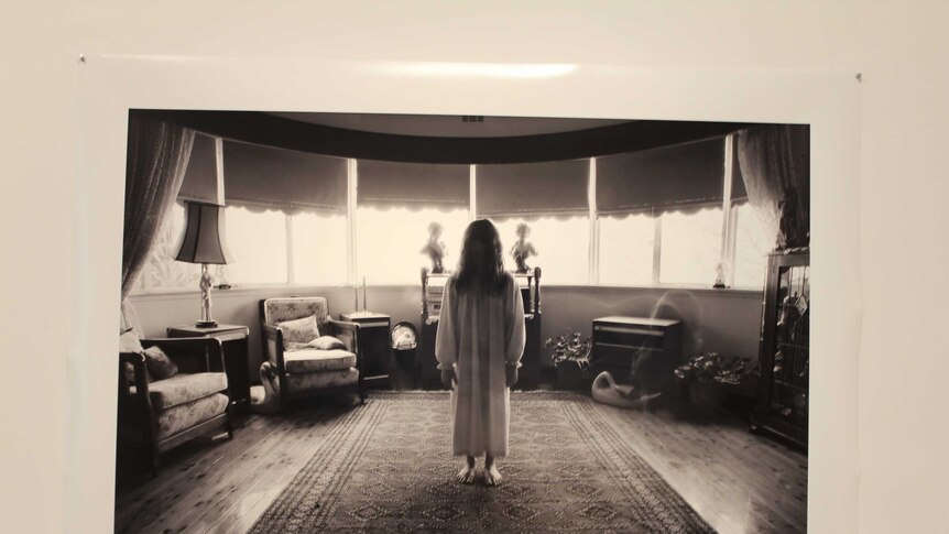 Photograph of a girl standing in a living room with her back to the camera