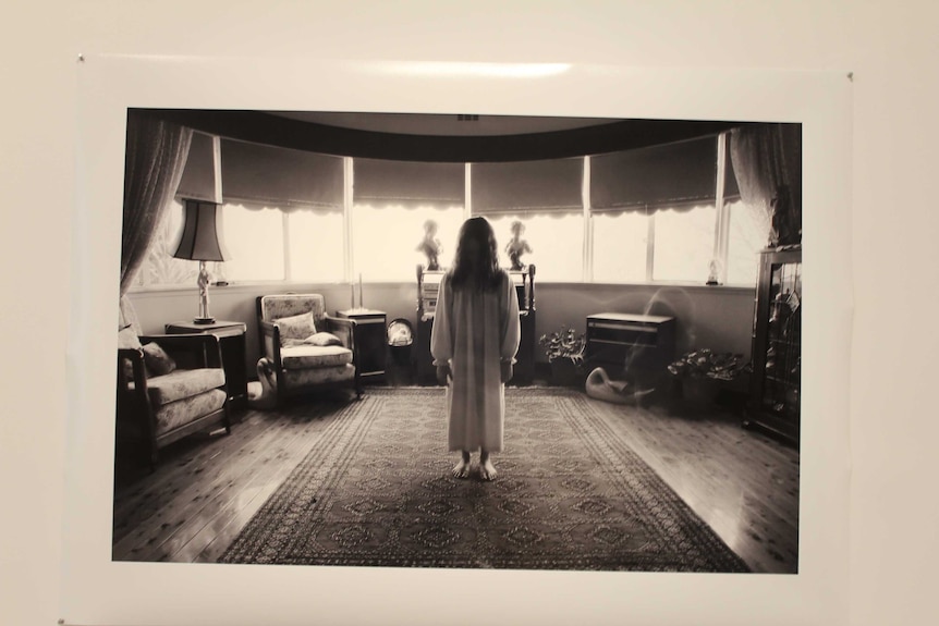 Photograph of a girl standing in a living room with her back to the camera