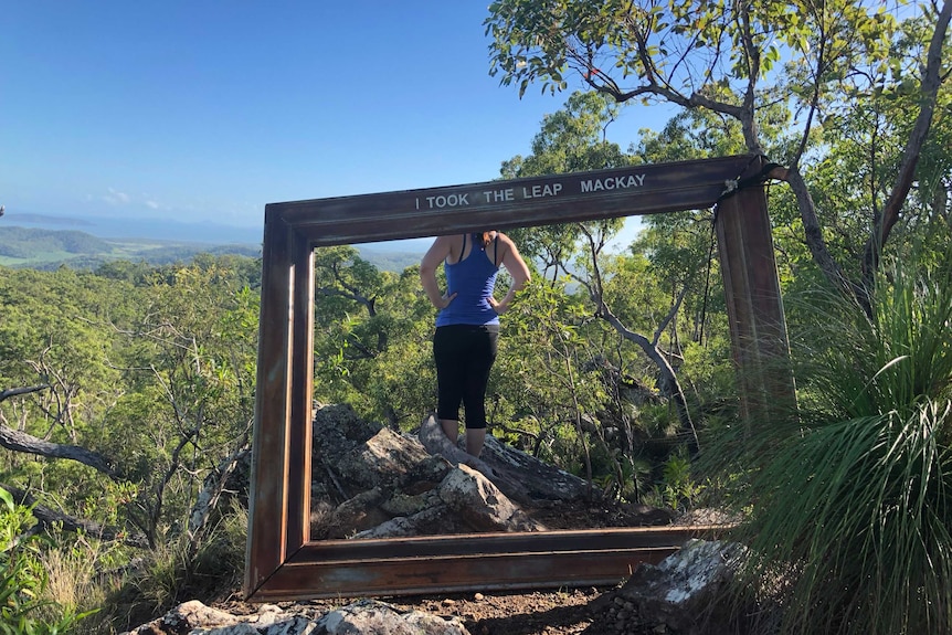 A woman standing at an outlook in front of a sign saying I took the leap