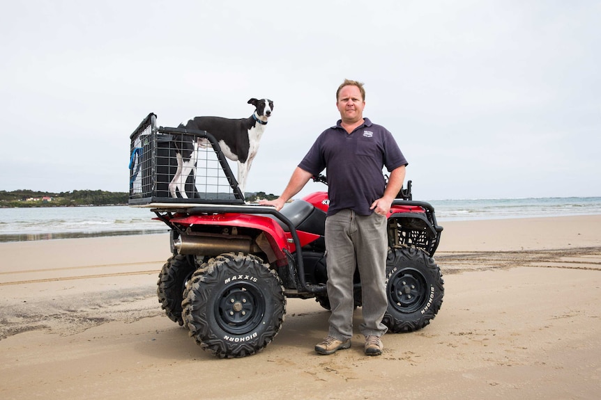 Greg Purton poses on a beach, his sits on a quad bike behind him.