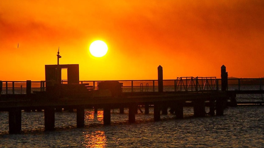 Sun in an orange sky overlooking a wharf