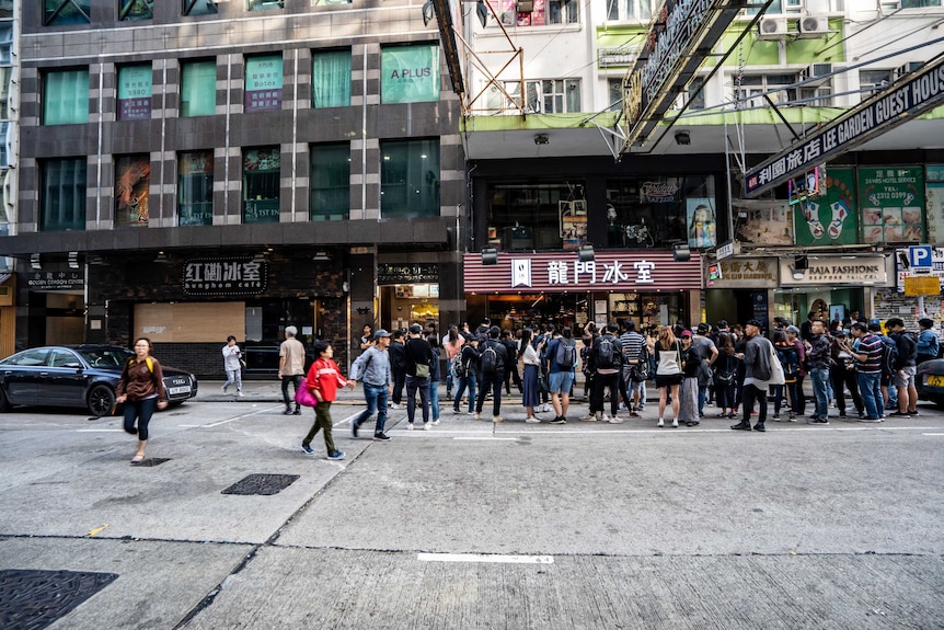 People line up around one shopfront, while the one next door is boarded up