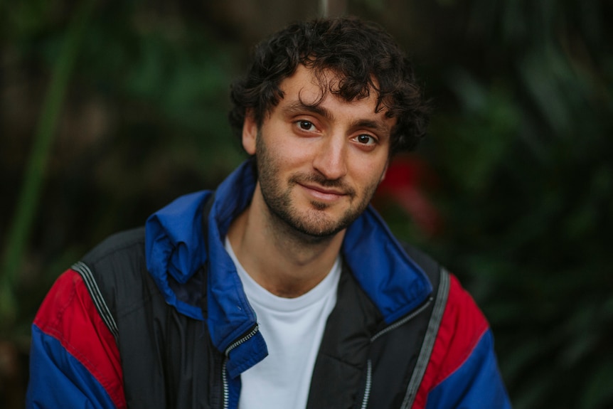 Man in his mid-20s Alexi Barnstone looking at camera wearing puffy electric blue jacket.