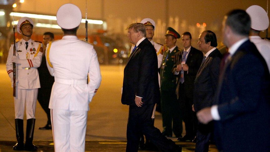 Donald Trump walks through a crowd of uniformed Vietnamese dignitaries, some in white uniforms carrying guns