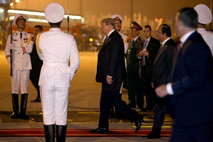 Donald Trump walks through a crowd of uniformed Vietnamese dignitaries, some in white uniforms carrying guns