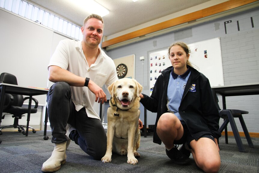A therapy dog sits between a teacher and student at lake Illawarra