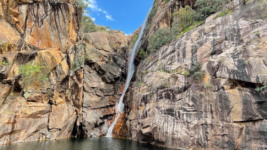 A waterfall running down steep rockfaces and into a pool, on a  sunny day.