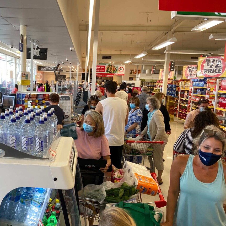 People in masks at a supermarket check-out area.