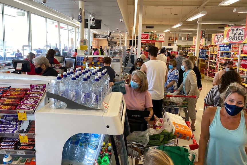 People in masks at a supermarket check-out area.