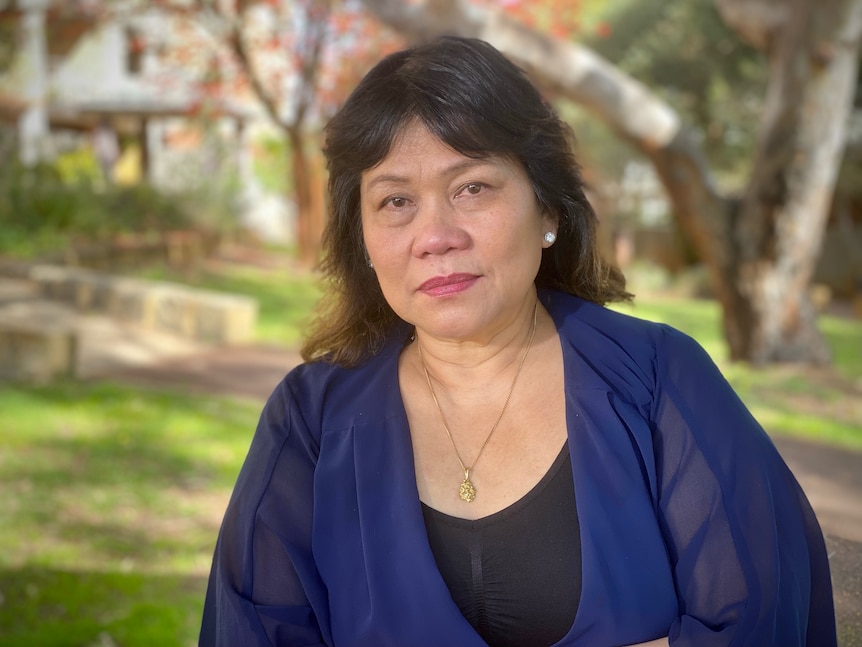 Female aged care worker standing in a park looking at camera not smiling.