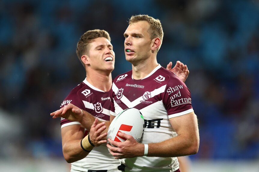 Two rugby league players come together in celebration after a try, with the scorer holding the ball