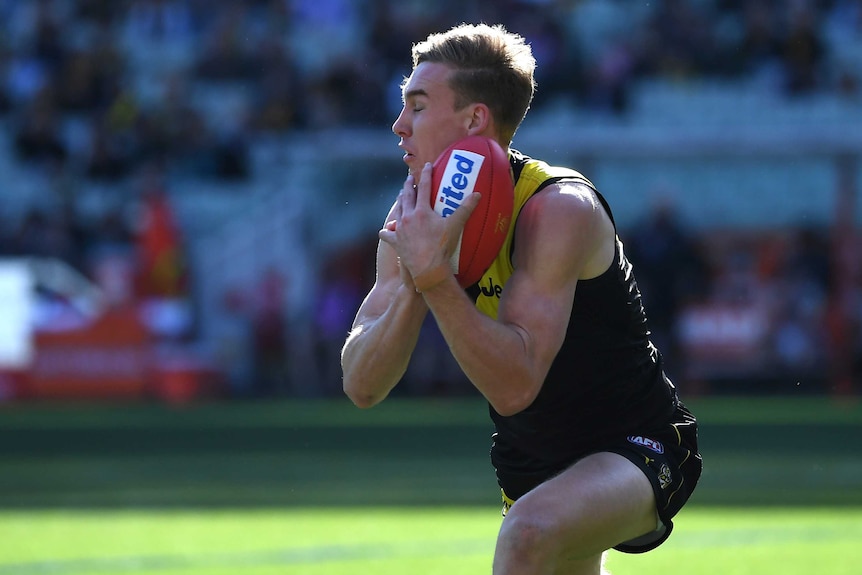 An AFL player marks the ball on one knee.