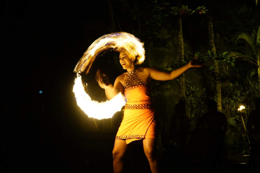 Moemoana Schwenke smiles as she twirls a large machete and flames make a ring of fire.