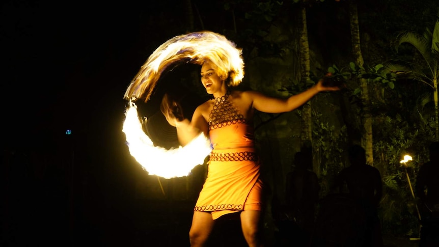 Moemoana Schwenke smiles as she twirls a large machete and flames make a ring of fire.