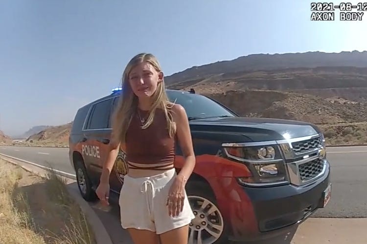 A young blonde woman crying next to a police car on a desert road