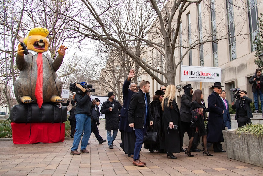 Crowds gather as Roger Stone walks into court and a big rat-like trump statue appears to the left.