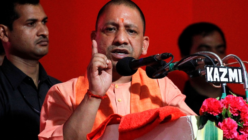 A man dressed in orange points his hands in the air at a podium.