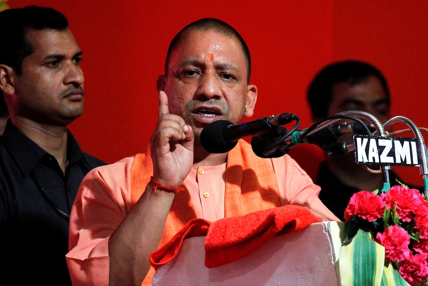 A man dressed in orange points his hands in the air at a podium.