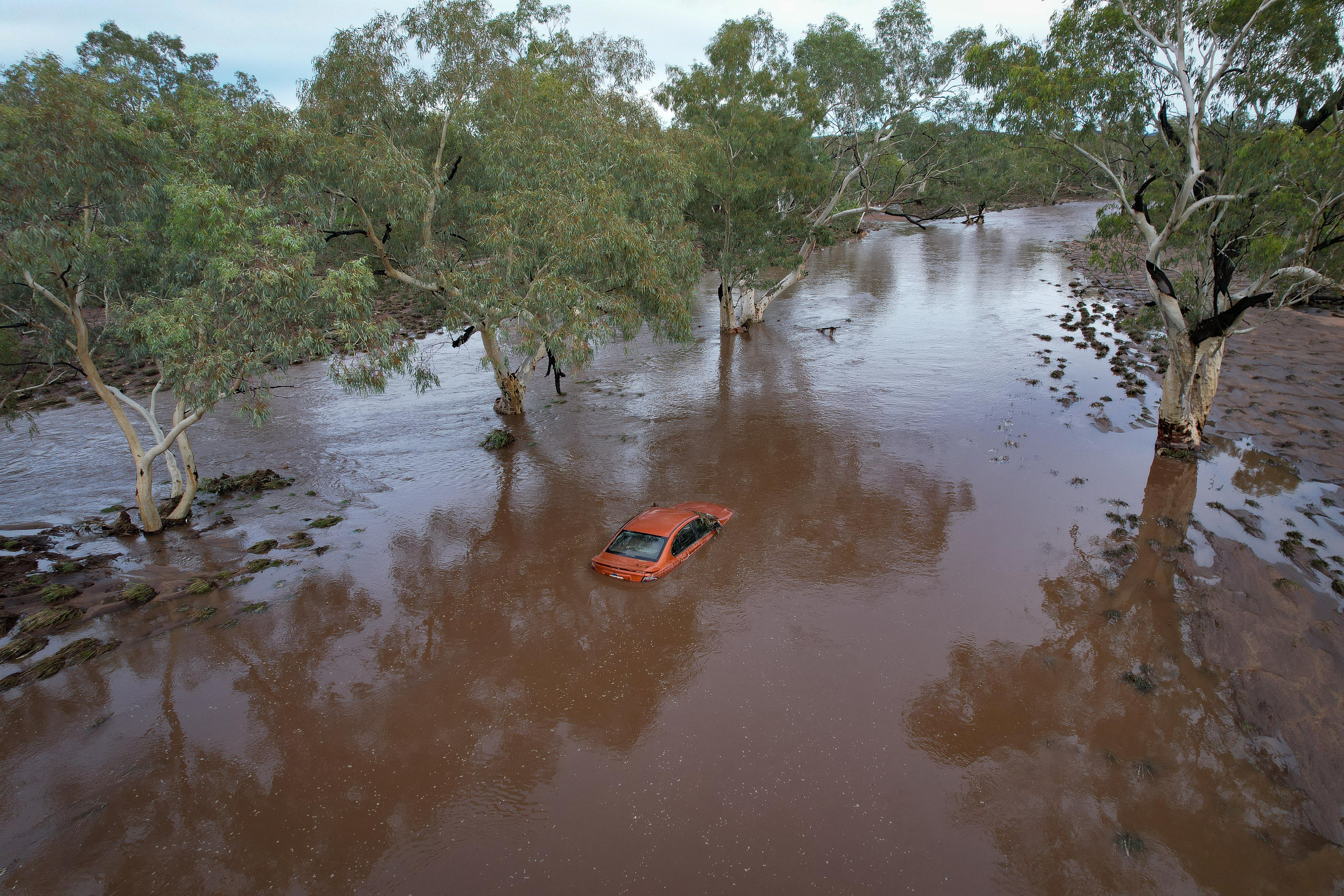 Um carro vermelho preso pelas águas marrons da enchente.