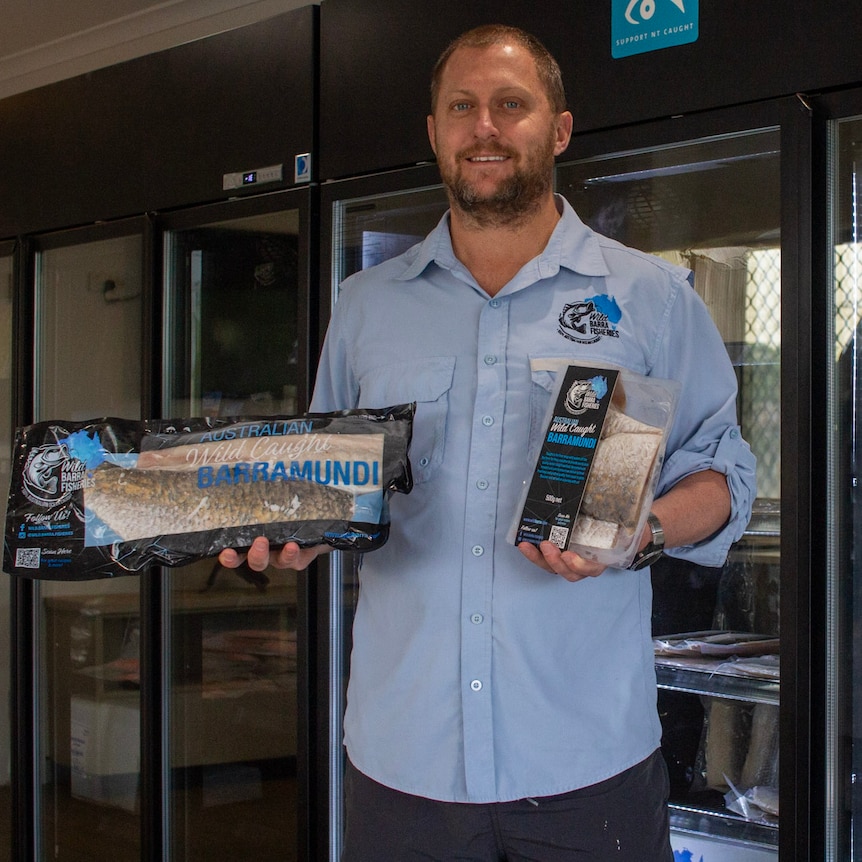 a man standing in front of a fridge, holding barramundi products.