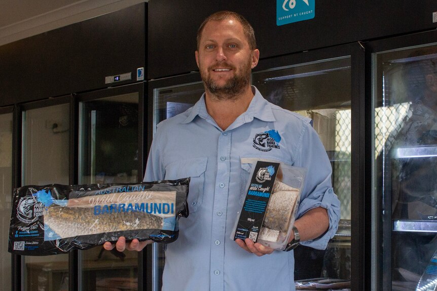 a man standing in front of a fridge, holding barramundi products.