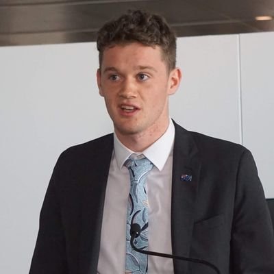 A young man, in a suit with a blue tie, speaks at a podium.