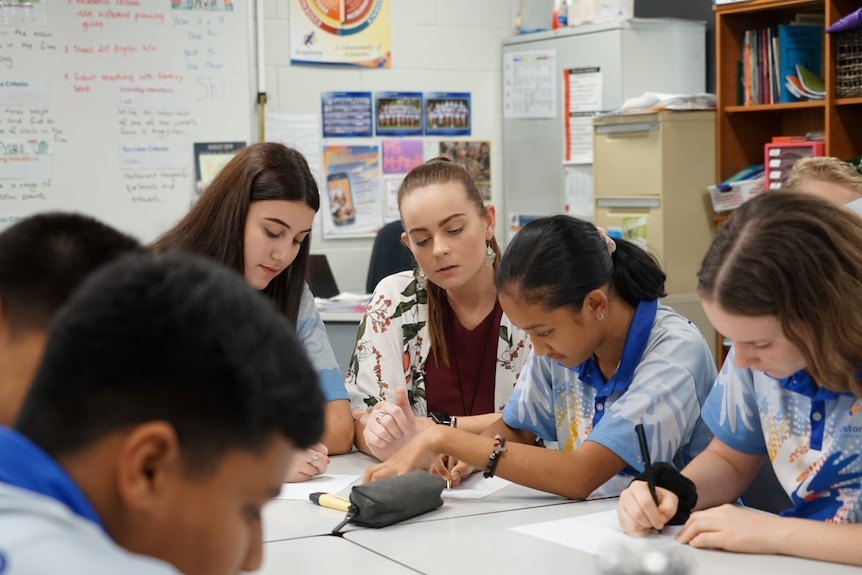 Students sit with their teacher in a classroom.