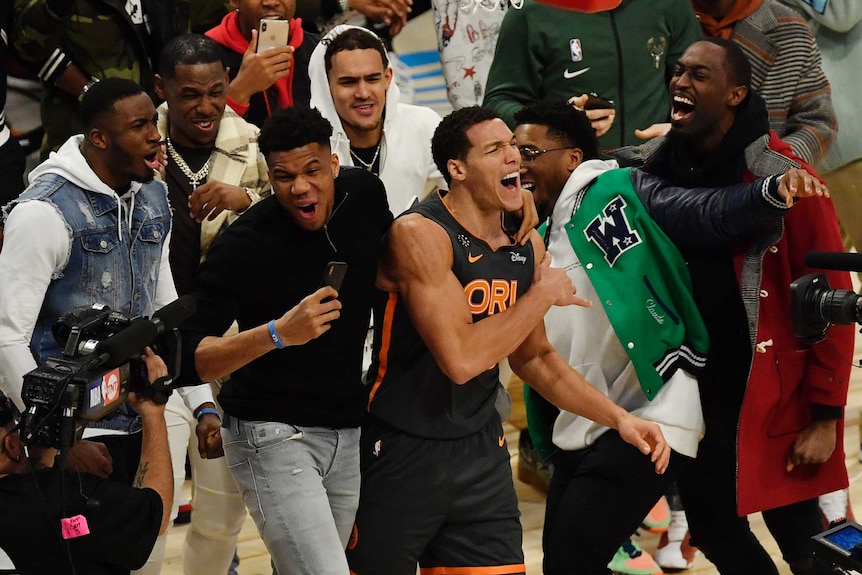 A number of NBA players in plain street clothes celebrate with Aaron Gordon, who's in his Magic kit.