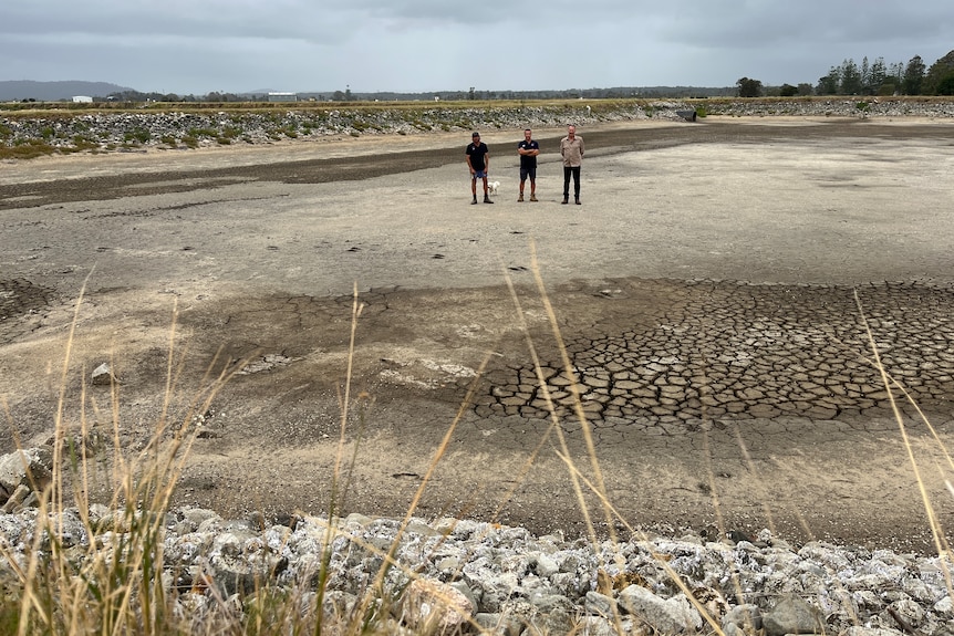 three men standing in middle of a dried out pond the size of a football oval