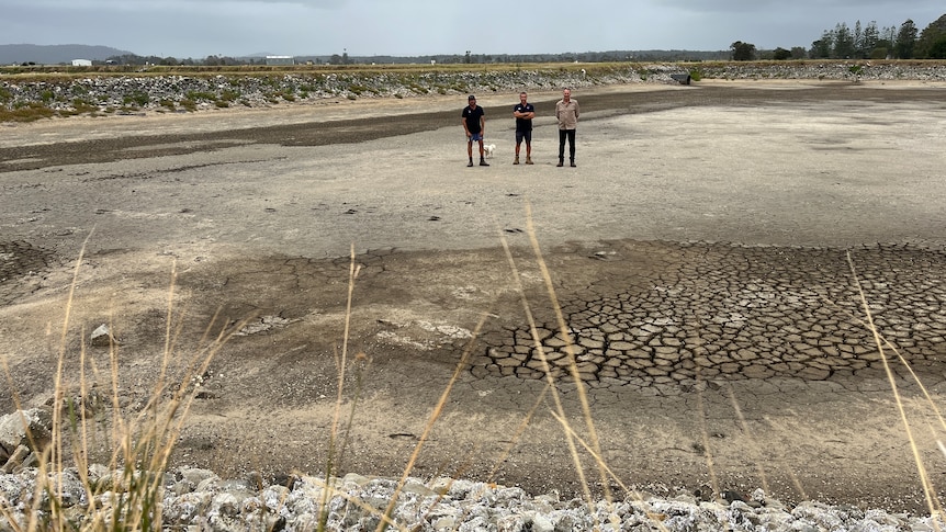 three men standing in middle of a dried out pond the size of a football oval