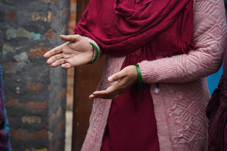 A close-up on a woman's hands. She is wearing maroon robes and pink cardigan