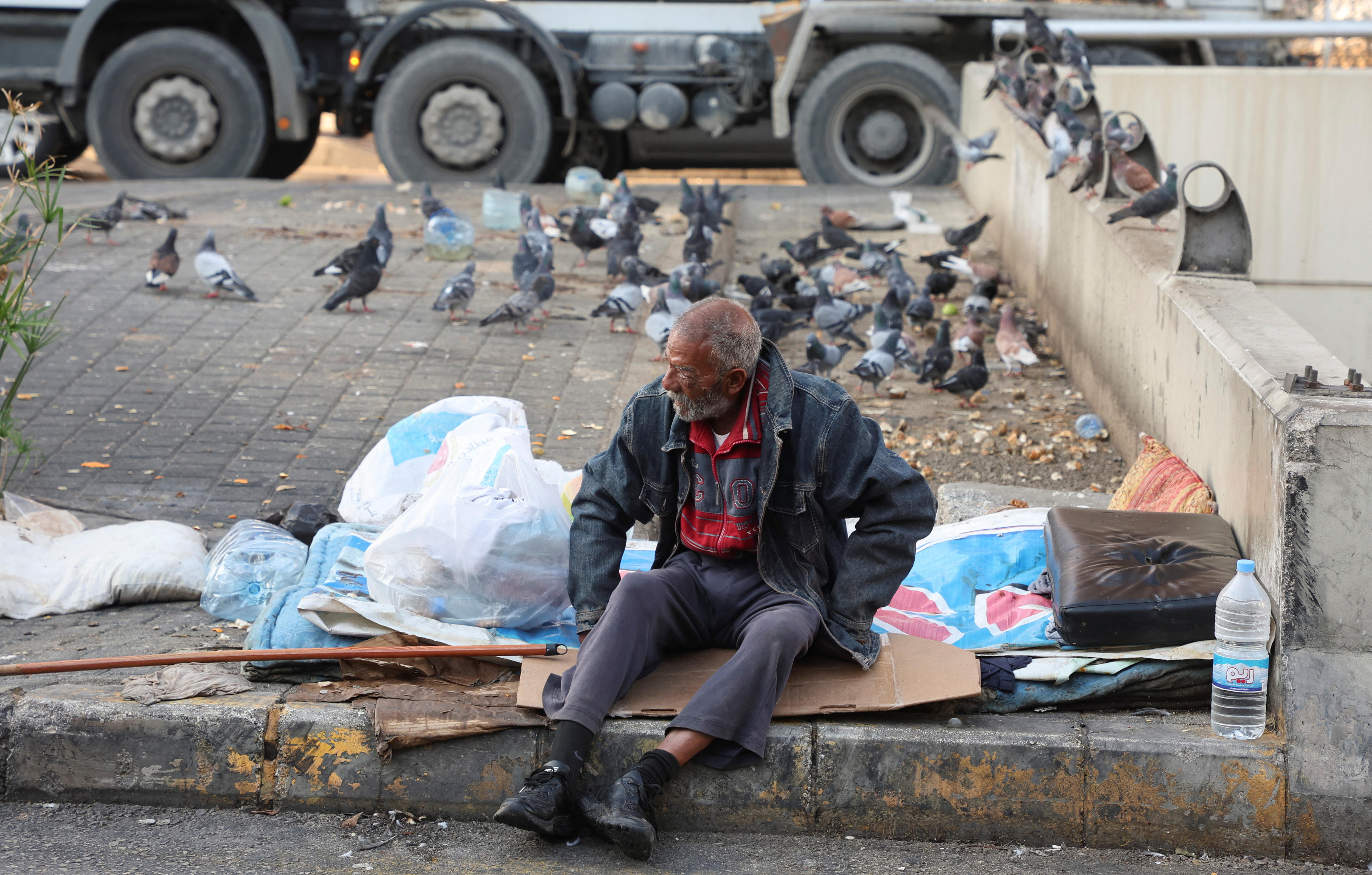 A homeless man sits on a curb along a street in Beirut.