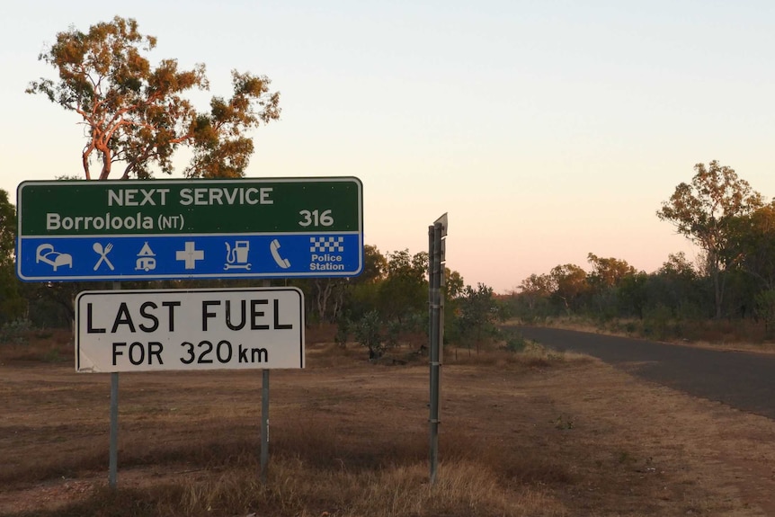 Road sign about next fuel stop on a deserted road at sunset
