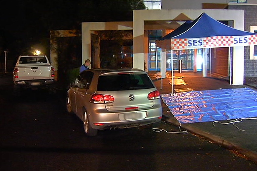 The white ute and silver hatchback are parked outside a police station, where a crime scene has been set up.