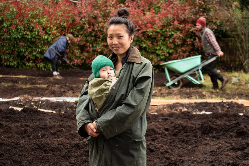 Rosie Lee holding a baby with gardeners in the background.