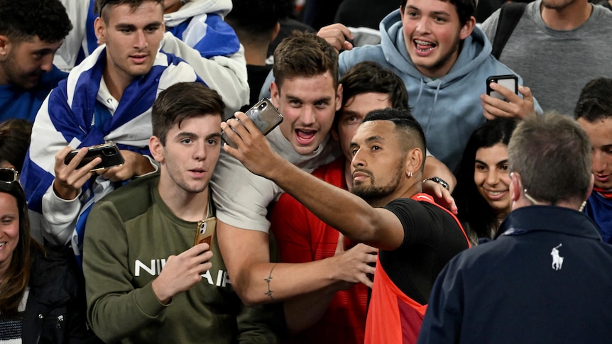 An Australian male tennis player poses with spectators for a selfie.